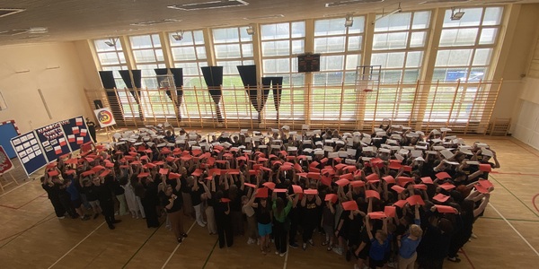 Uczniowie z białymi i czerwonymi kartkami nad głowami tworzą flagę