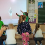 Uczniowie ćwiczą przed ekranem dużego monitora wiszącego na ścianie