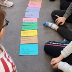 Uczniowie układają na podłodze kolorowe karteczki z prawami dziecka