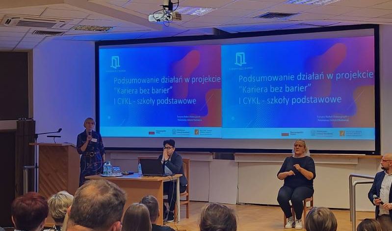 Konferencja - prowadzący na tle prezentacji