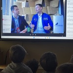 Uczniowie uczestniczą w ciekawym spotkaniu dzięki nowoczesnym technologiom (przed ekranem interaktywnym)